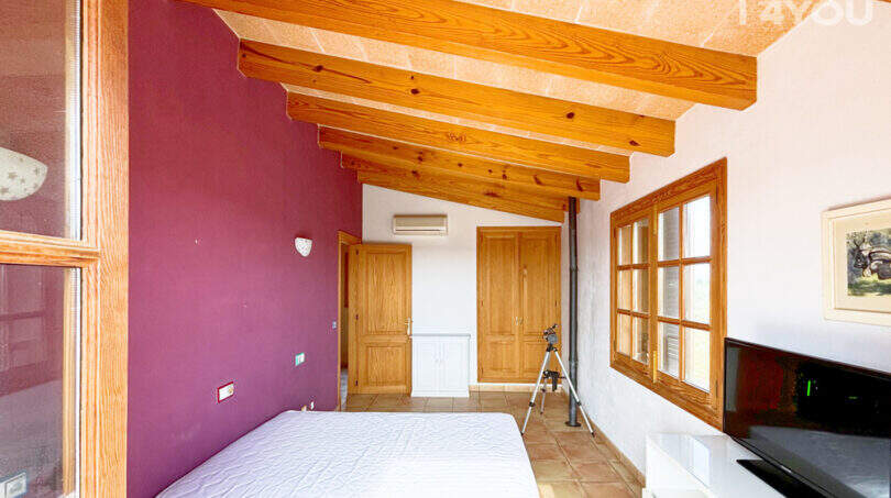 Schlafzimmer der Finca in Ses Salines mit Holzbalkendecke, lila Akzentwand und Terrakottaboden