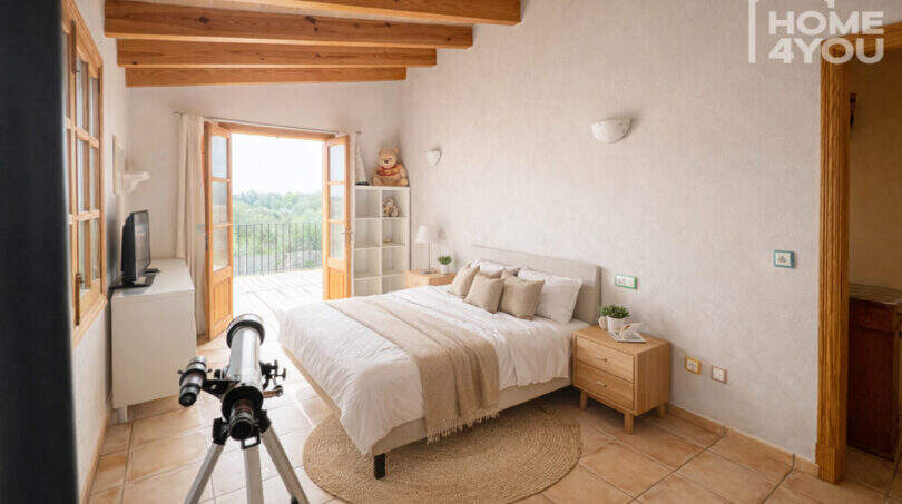 Helles Schlafzimmer der Finca in Ses Salines mit Holzbalkendecke, Doppelbett, Balkon und Natursteinboden.