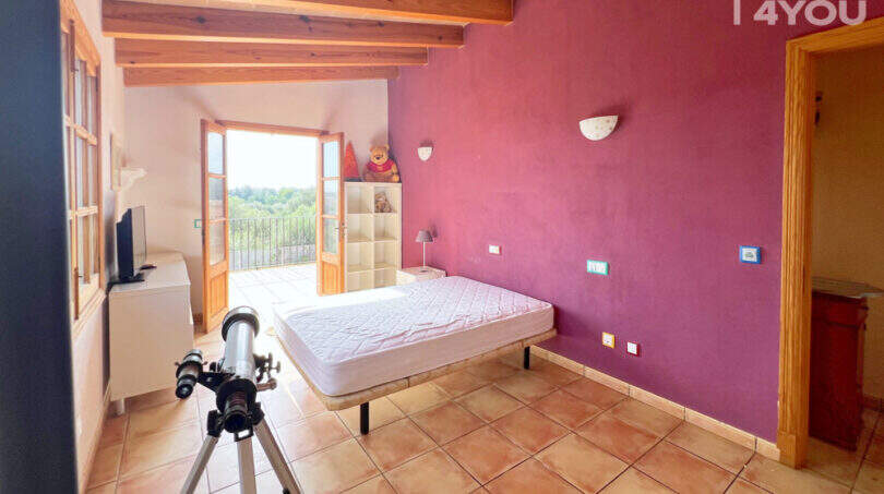 Schlafzimmer mit lila Wand, Holzbalkendecke, Balkonzugang & Meerblick in Finca Ses Salines