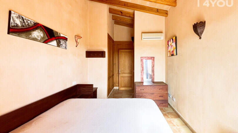 Schlafzimmer der Finca Ses Salines mit Holzbalkendecke, Klimaanlage, Kommode und rustikalem Charme.