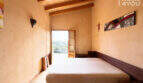 Schlafzimmer der Finca in Ses Salines mit Holzbalkendecke, Doppelbett und Balkontür mit Naturblick.