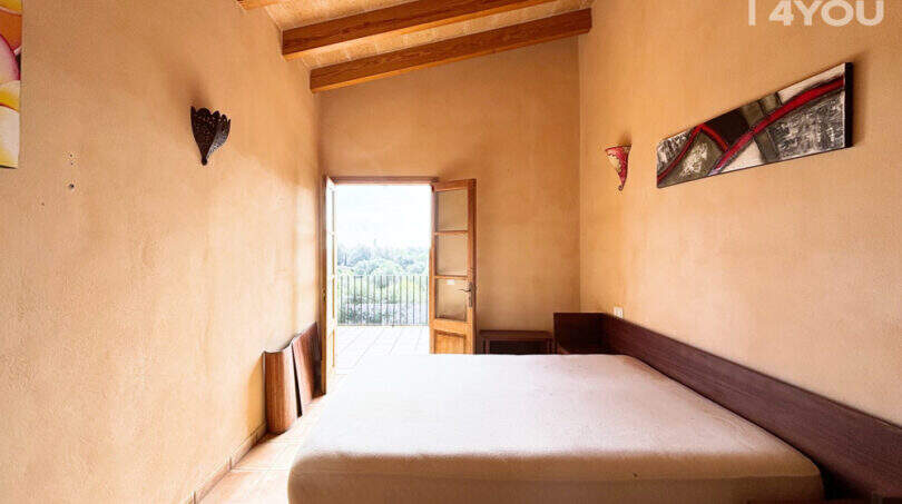 Schlafzimmer der Finca in Ses Salines mit Holzbalkendecke, Doppelbett und Balkontür mit Naturblick.