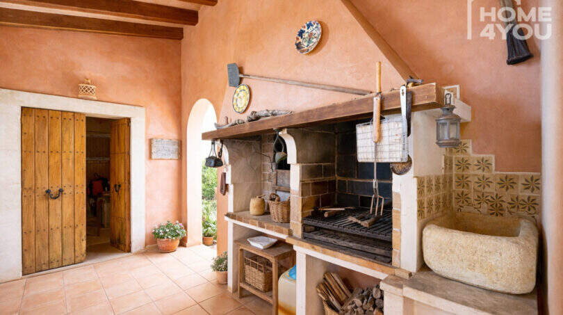 Rustikale Außenküche mit offenem Grillkamin, Naturstein-Spülbecken und Holzbalkendecke der Finca in Ses Salines.