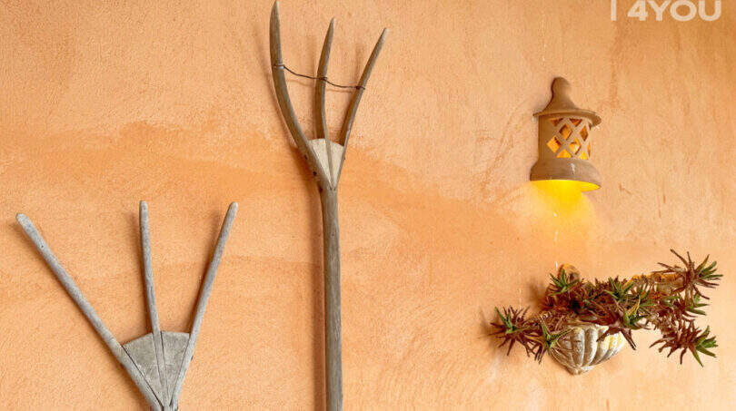 Rustikale Wanddekoration mit Holzgabeln, Laternenleuchte und Wandpflanzgefäß an orangefarbener Finca-Außenwand