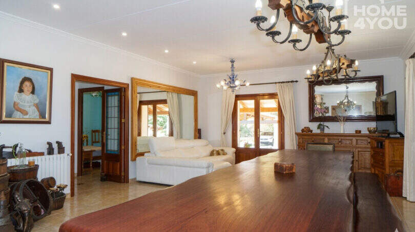 Geräumiges Wohnzimmer der Finca mit massivem Holztisch, Kronleuchtern und weißen Ledersofas in Santa Margalida.