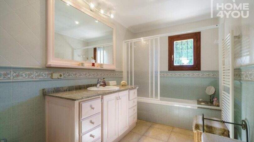 Helles Badezimmer der Finca mit Badewanne, Dusche, Waschtischunterschrank und dekorativen Fliesenbordüren.