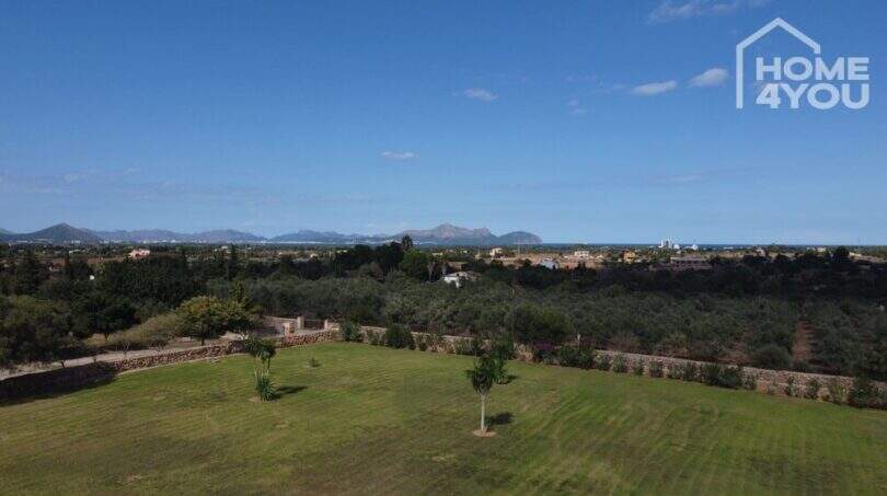 Weitläufiger Garten der Finca in Santa Margalida mit Palmen, Steinmauern und Bergpanorama