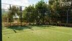 Privater Padelplatz mit Kunstrasen, Glaswänden und Metallgitter-Umzäunung, umgeben von mediterraner Vegetation.