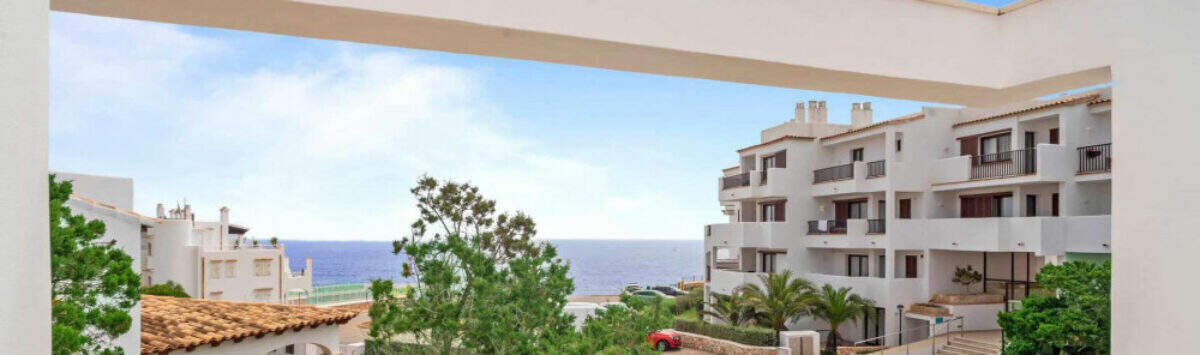 Penthouse-Terrasse in Cala d'Or mit Meerblick, weißen Fassaden und mediterranem Grün unter blauem Himmel.