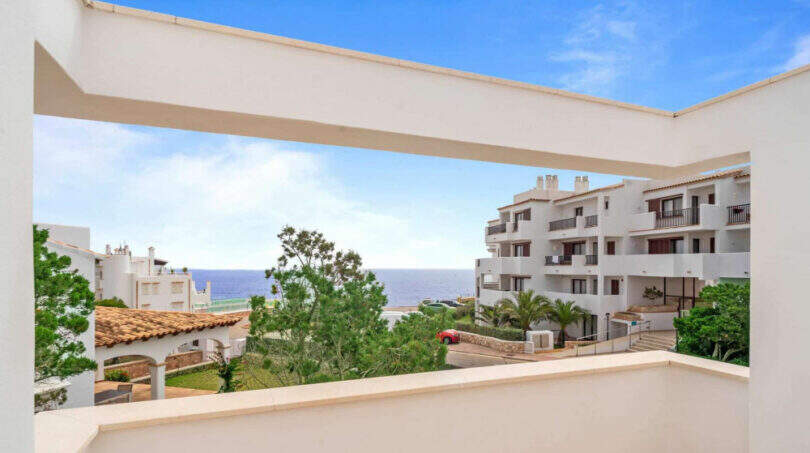 Penthouse-Terrasse in Cala d'Or mit Meerblick, weißen Fassaden und mediterranem Grün unter blauem Himmel.