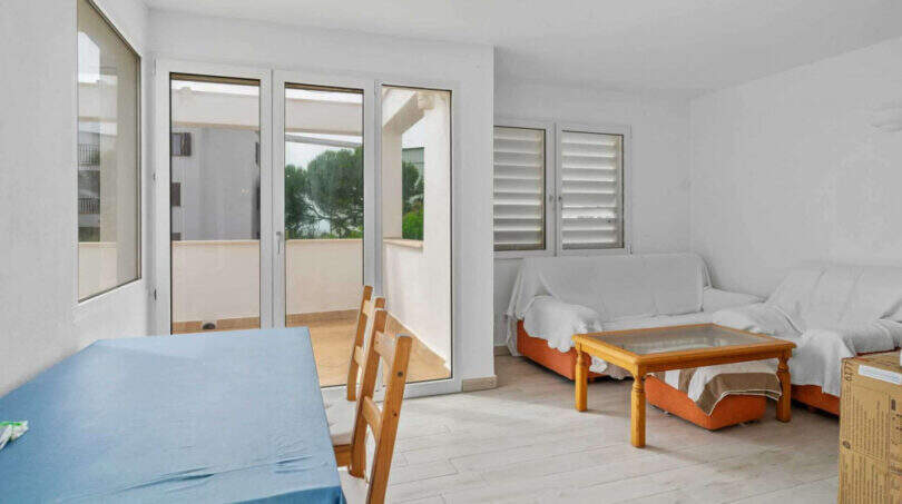 Helles Wohnzimmer des Penthouses in Cala d'Or mit Holzboden, Sofa, Glastisch und Terrassenzugang mit Meerblick.