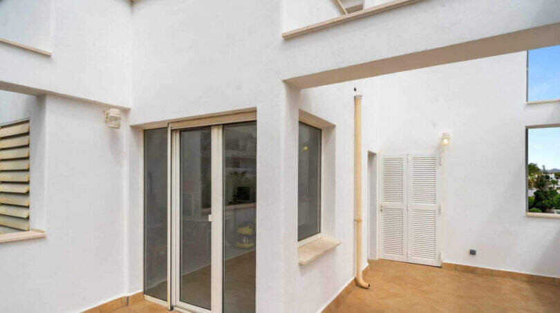 Überdachte Terrasse des Penthouses in Cala d'Or mit Schiebetüren, weißen Wänden und Fliesenboden