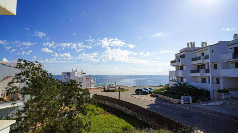 Außenansicht Penthouse Cala d'Or: Weißes Apartmentgebäude mit Meerblick, Parkplatz und gepflegter Grünanlage.