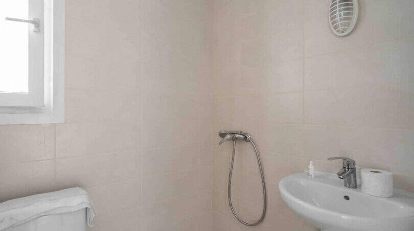 Helles Badezimmer im Penthouse Cala d'Or mit Dusche, Waschbecken, WC und Fenster, cremefarbene Fliesen