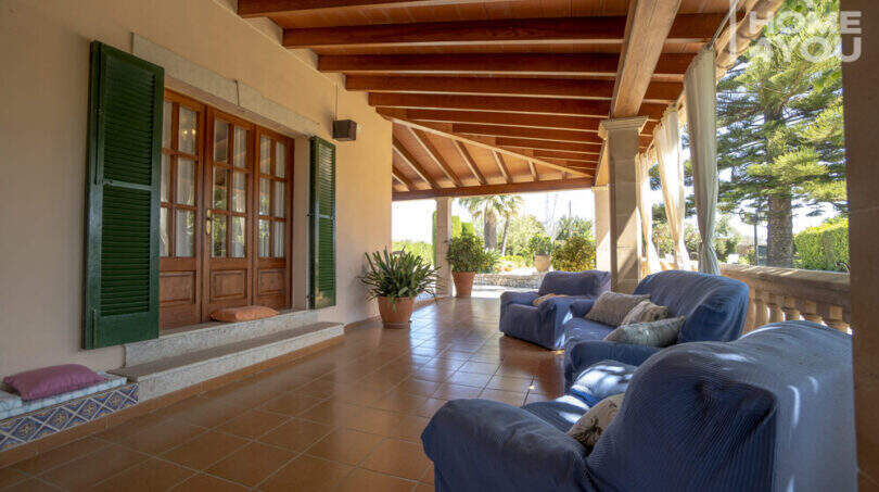 Überdachte Terrasse der Finca Lloseta mit blauen Sofas, Holzbalkendecke und Blick in den mediterranen Garten.