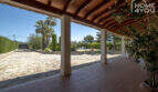Überdachte Terrasse der Finca in Lloseta mit Holzdecke, Steinboden und Blick auf Pool und Gartenanlage.
