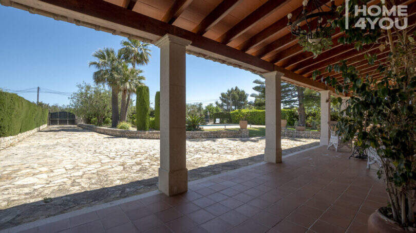 Überdachte Terrasse der Finca in Lloseta mit Holzdecke, Steinboden und Blick auf Pool und Gartenanlage.