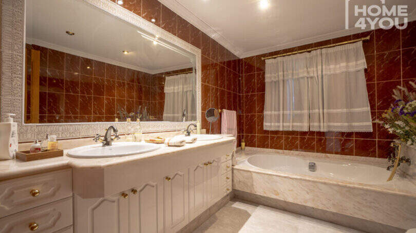 Luxusbad mit rotem Marmor, Doppelwaschbecken, weißem Unterschrank und eleganter Einbaubadewanne in Finca Lloseta