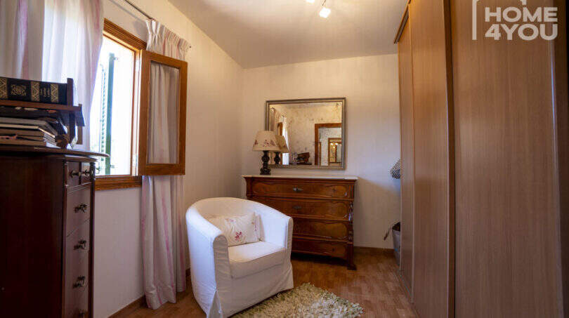 Gemütliches Schlafzimmer der Finca Lloseta mit weißem Sessel, Holzkommode, Spiegel und Einbauschrank.