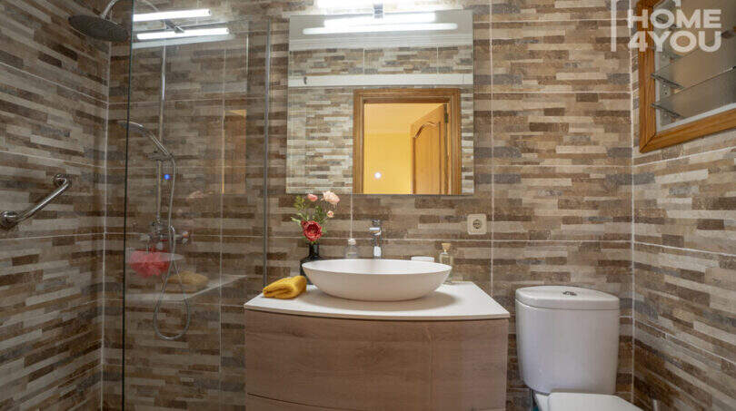 Modernes Badezimmer der Finca in Lloseta mit Dusche, Waschtisch, WC und Naturstein-Wandfliesen.