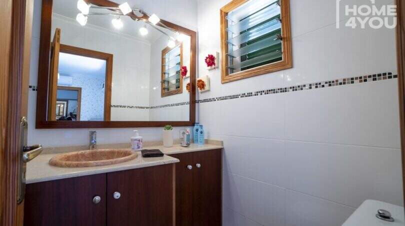 Badezimmer der Finca in Lloseta mit Holzunterschrank, Marmorbecken, beleuchtetem Spiegel und Jalousie-Fenster.