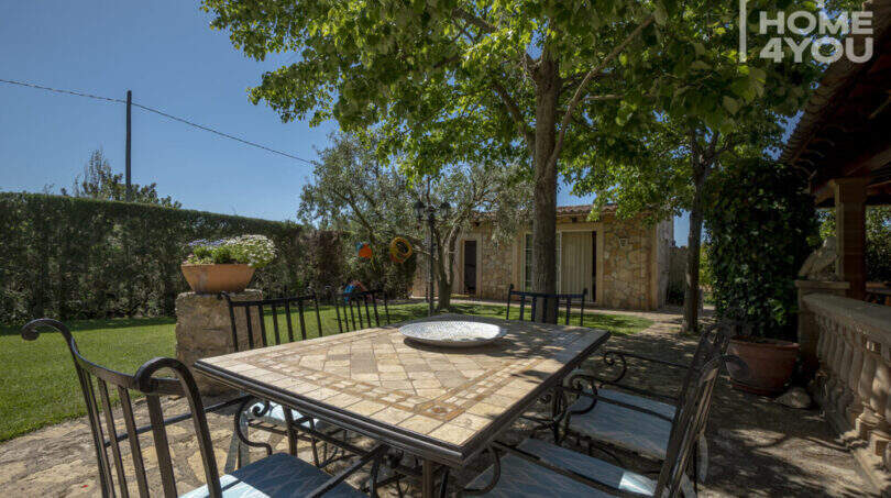 Mediterrane Finca Lloseta: Sonnige Terrasse mit Mosaiksteintisch, Schmiedeeisenstühlen und schattenspendenden Bäumen.