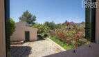 Blick aus Fenster auf mediterranen Innenhof mit Nebengebäude, roter Bougainvillea und grüner Landschaft in Lloseta