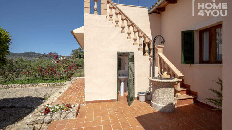 Außenbereich der Finca Lloseta: Terrasse mit Terrakottafliesen, Außentreppe, Brunnen und Gartenblick