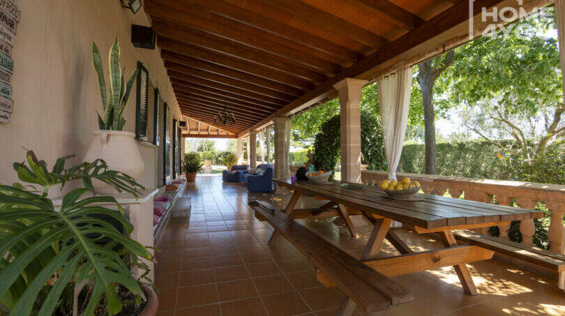 Überdachte Terrasse der Finca in Lloseta mit Holzdecke, Picknicktisch und Blick in den mediterranen Garten.