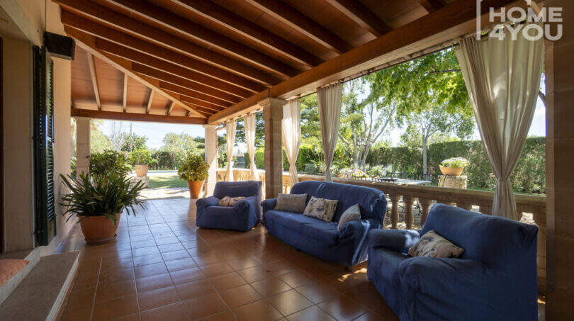 Überdachte Terrasse der Finca Lloseta mit blauen Sofas, Holzbalkendecke und Blick in den Garten.