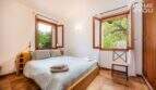 Schlafzimmer der Finca Campanet mit Doppelbett, Holzrahmen-Fenstern und Blick ins mediterrane Grün