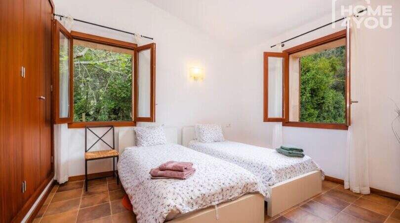 Helles Schlafzimmer der Finca in Campanet mit zwei Einzelbetten, Holzschränken und Fenstern mit Naturblick.