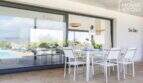 Covered terrace of the finca Son Amer with white dining table, pool view and large glass front, Sa Pobla
