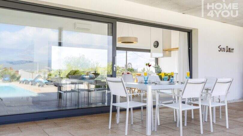 Covered terrace of the finca Son Amer with white dining table, pool view and large glass front, Sa Pobla
