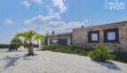 Exterior view Mediterranean finca Sa Pobla: natural stone wall, palms, white gravel path and pool in the background.