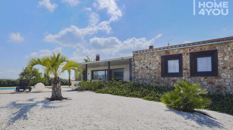 Exterior view Mediterranean finca Sa Pobla: natural stone wall, palms, white gravel path and pool in the background.