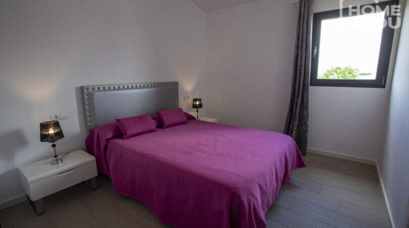 Bedroom of the finca in Sa Pobla with double bed, purple bedding, wooden floor and window with garden view.