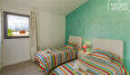 Bright bedroom with 2 single beds, colorful striped bedding, turquoise accent wall and mountain view through window.