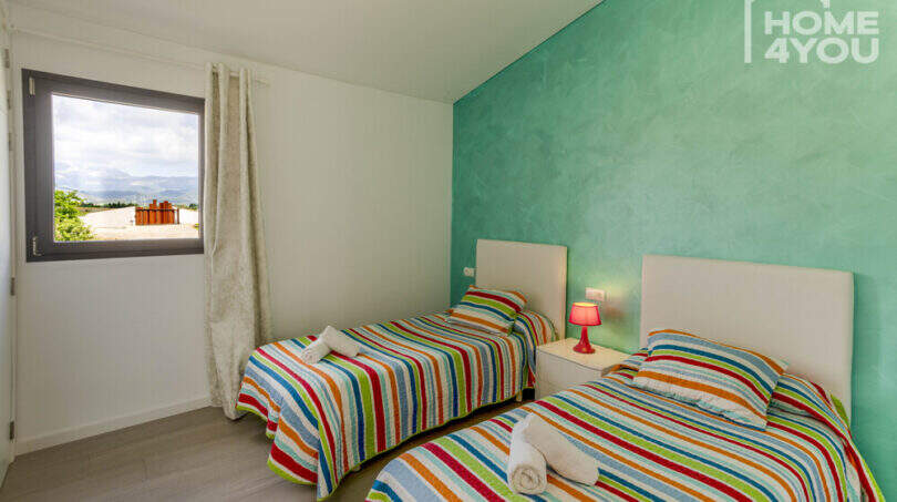 Bright bedroom with 2 single beds, colorful striped bedding, turquoise accent wall and mountain view through window.