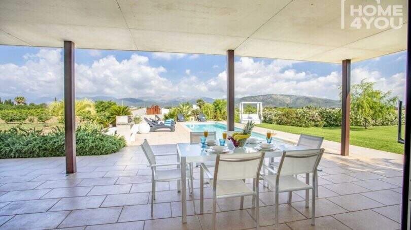 Covered terrace with white dining table, view of pool and mountain panorama of the finca in Sa Pobla