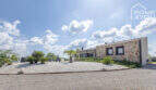 Exterior view Mediterranean finca Sa Pobla: natural stone house with gravel garden, palms and lounge area under blue sky.
