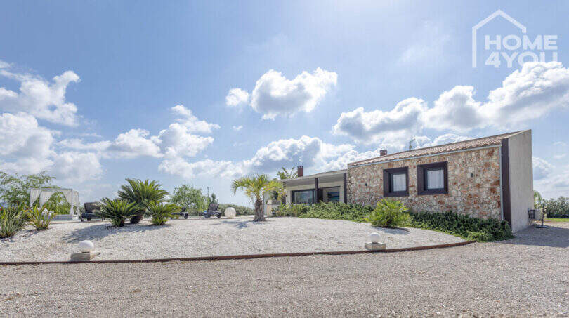 Exterior view Mediterranean finca Sa Pobla: natural stone house with gravel garden, palms and lounge area under blue sky.