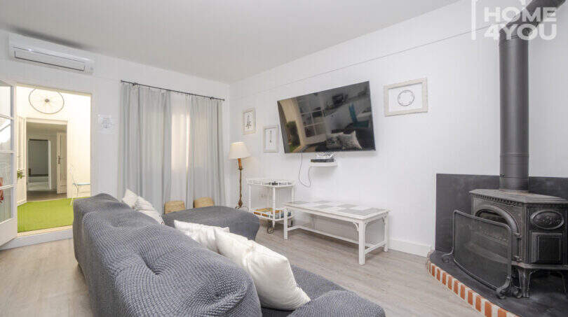 Helles Wohnzimmer mit grauem Sofa, Kaminofen, Wandtv und Klimaanlage im Stadthaus Maria de la Salut