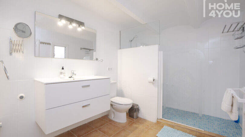 Helles Badezimmer mit weißem Waschtischunterschrank, Dusche mit Mosaikboden, WC und großem Spiegel