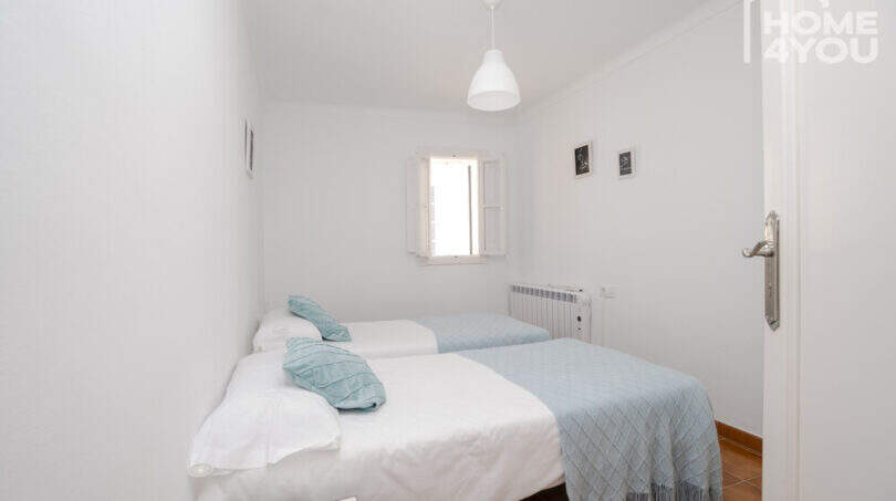Helles Schlafzimmer mit zwei Einzelbetten, türkisen Kissen, Heizkörper und Fenster im Stadthaus Maria de la Salut