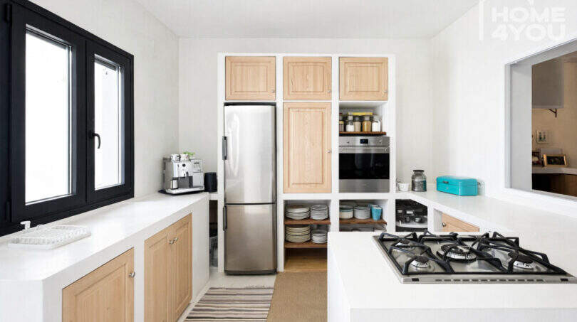 Moderne Küche im Ibiza-Stil mit Holzfronten, Edelstahlkühlschrank, Gaskocher und weißen Arbeitsflächen.