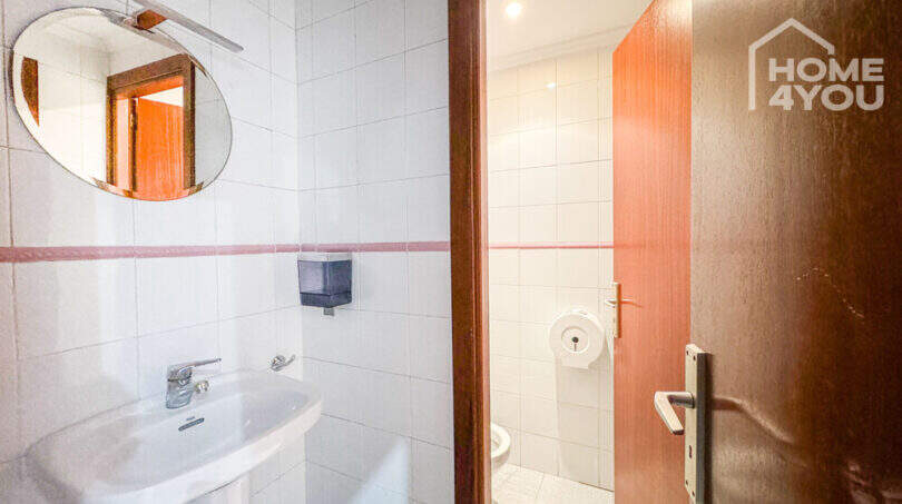 WC-Bereich des Geschäftslokals in Felanitx mit Waschbecken, Spiegel, weißen Fliesen und Holztür