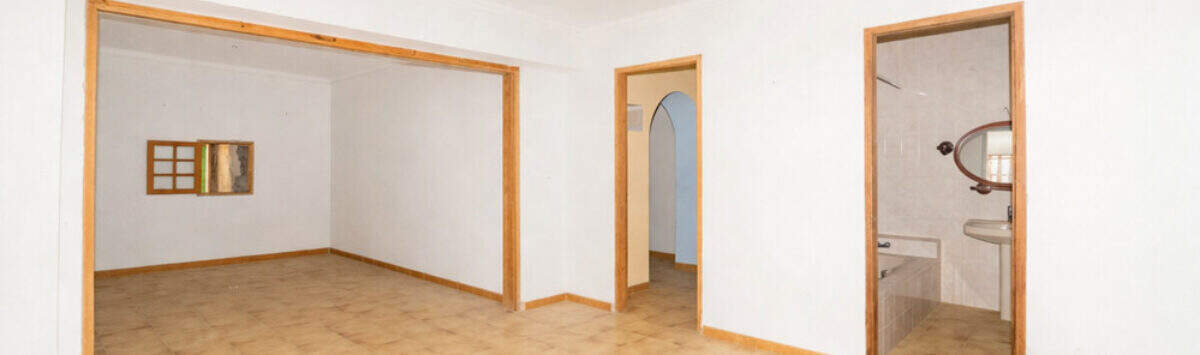 Empty living space with tiled floors, wooden frame doors, bathroom view and passage in the multi-family house Felanitx
