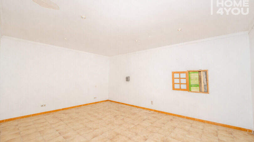 Empty living space with tiled floor, white walls and small wooden window in the multi-family house Felanitx