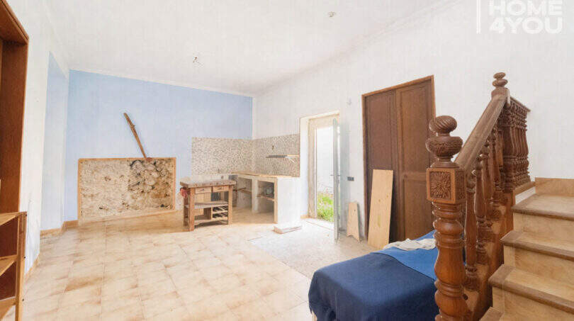 Renovation-needed living space with wooden staircase, tiled floors and blue accent wall in the multi-family house Felanitx